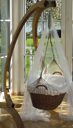 a hammock hanging from a wooden frame in front of a window with sheer curtains