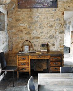 an old fashioned desk and chair in a stone walled room with a painting on the wall