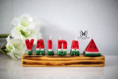 watermelon candles spelling the word vada on a wooden board with flowers in the background