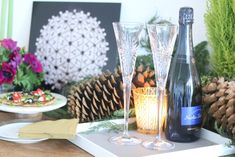 two wine glasses sitting on top of a table with pine cones and other decorations behind them