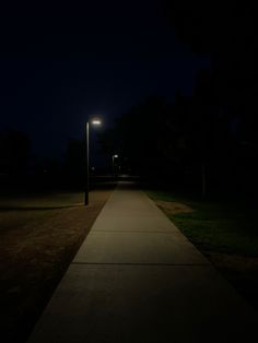 an empty sidewalk at night with street lights in the distance and grass on both sides