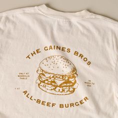 Show off your support for one of the best burgers in town with this classic ivory tee! Inspired by the fan-favorite Gaines Brothers Burger at Magnolia Table, this white tee features a playful, contrasting burger graphic that reads THE GAINES BROS ALL-BEEF BURGER. Restaurant Tshirt Designs, Burger Graphic, The Best Burgers, Best Burgers, Magnolia Table, Beef Burger, Aime Leon Dore, Shirt Design Inspiration, Good Burger