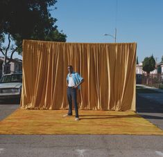 a man standing in front of a yellow curtain on top of a rug next to a street