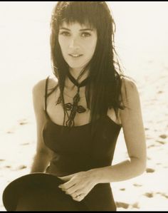 a woman sitting in the sand with her legs crossed and wearing a black tank top