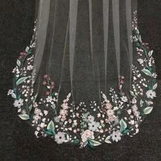 an embroidered veil with flowers and leaves on the side, hanging from a black background