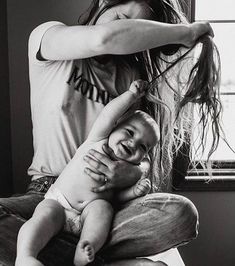 a woman combs her baby's hair while she sits on the floor in front of a window