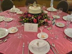 the table is set for a formal dinner with pink linens and white plates, silverware