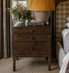 a lamp on top of a wooden dresser next to a bed with pillows and blankets