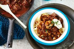 a bowl of pasta with meat and sauce next to a pot of stew on a table