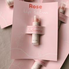 three bottles of rose lip balm sitting on top of pink paper