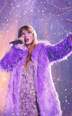 a woman in a purple fur coat holding a microphone and singing into the air with her arms outstretched