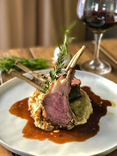 a white plate topped with meat and gravy next to a glass of wine