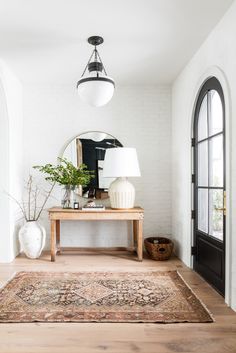 a living room with a rug, table and lamp on the floor next to an arched doorway