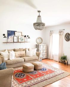 An eclectic living room with poufs boasts white walls and a golden wood floor. A wood shelf hangs between two small black sconces above a beige sofa. The beige poufs sit on a red rug on a beige mat, while a white cabinet is pushed into the corner...   Image: interiorswag