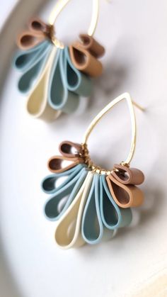 two pairs of earrings are sitting on a white plate and one pair is gold, the other blue