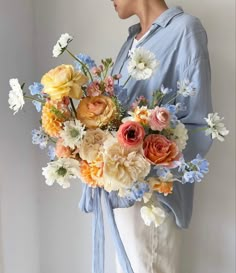 a woman holding a large bouquet of flowers in her hands and wearing a blue shirt