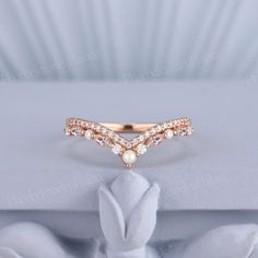 a rose gold ring with white pearls and diamonds on the side, sitting on top of a pillow