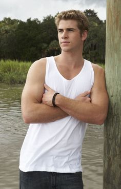 a young man standing next to a body of water wearing a white shirt and black watch