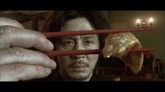 a man holding chopsticks in front of his face with food sticking out of them