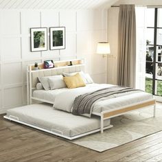 a white bed sitting on top of a hard wood floor next to a large window