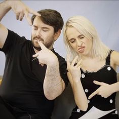 a man and woman sitting next to each other pointing at something on their finger fingers