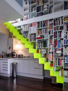 a kitchen with white cabinets and green stairs leading up to the top floor, next to a bookshelf full of books