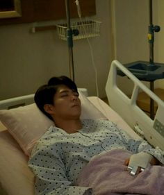 a young man laying in a hospital bed next to an iv machine and holding a remote control