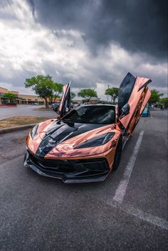 an orange and black sports car parked in a parking lot with its doors open on a cloudy day