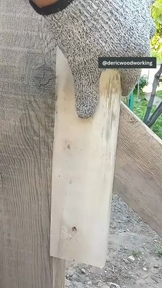 a person holding a piece of wood up to the side of a wooden fence post