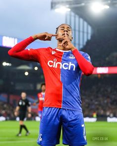 a man standing on top of a soccer field holding his hand to his face while wearing a red and blue uniform