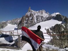 a man standing on top of a snow covered mountain holding a red white and black flag