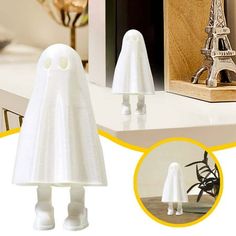 two white plastic ghost figurines sitting on top of a table next to a wooden box with an eiffel tower in the background