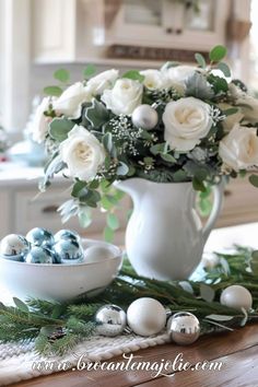 white roses and greenery in a vase on a table with silver baubies