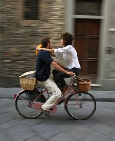 two men riding on the back of a bicycle