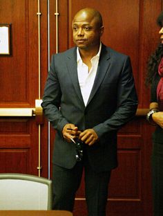 a man standing in front of a wooden paneled wall with two women behind him