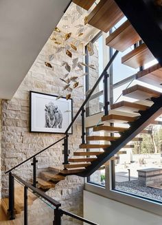 a stair case with wooden handrails next to a stone wall and glass windows