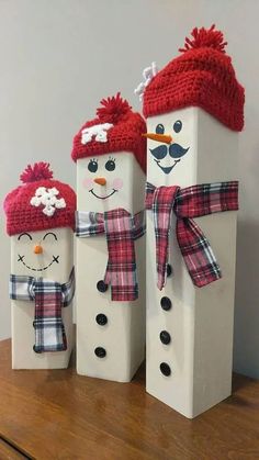 three snowmen with hats and scarfs on top of a wooden table next to each other