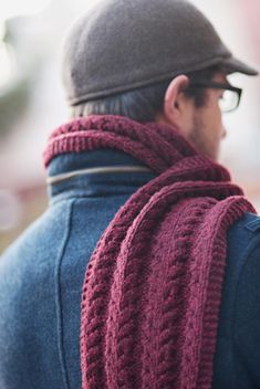 a man wearing a knitted scarf and hat looking off into the distance with his hand on his hip