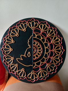 a black plate with gold and red beaded designs on the top, sitting on a person's lap