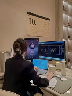 a woman sitting at a desk with two laptops and a desktop computer on it