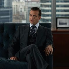 a man in a suit and tie sitting on a chair with a city view behind him