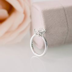 a diamond ring sitting on top of a box next to a pink rose and flower