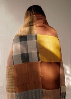 a woman is wrapped in a multicolored plaid blanket with buttons on the back