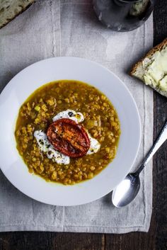 a white plate topped with lentula soup next to bread and a glass of wine