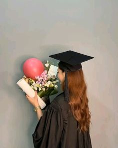 a woman wearing a graduation cap and gown holding a bouquet of flowers in front of her face