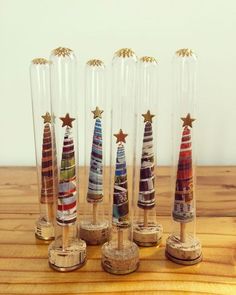 four glass tubes with different colored christmas trees in them on a wooden table top next to corks