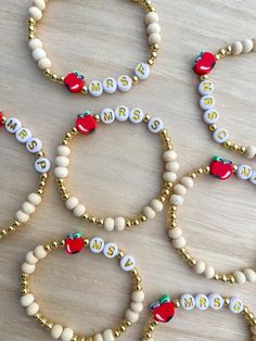 several beaded bracelets with apples and name beads are arranged on a wooden surface