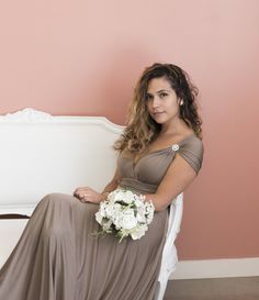 a woman in a long dress sitting on a white chair with flowers and a bouquet