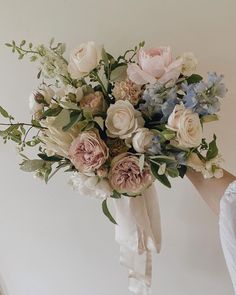 a bridal bouquet being held up by someone's hand on a white wall