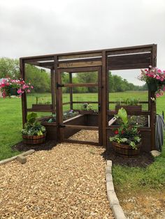 a wooden structure with plants in it on the side of a grassy field next to flowers